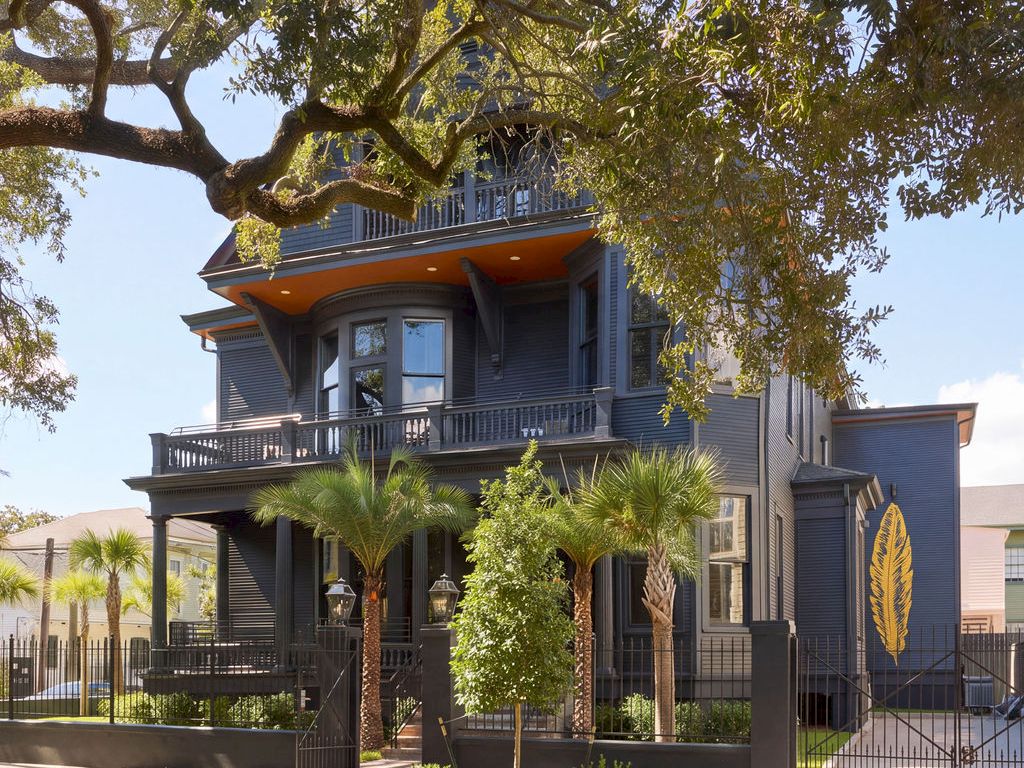 A large, three-story blue building with balconies and a fenced yard with palm trees.