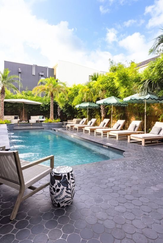 An outdoor resort pool with lounge chairs and umbrellas, surrounded by lush green bamboo and palm trees under a blue sky.