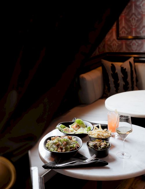 A restaurant table set with multiple bowls of food, salad, breadsticks, and drinks by a booth.