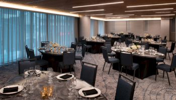 The image shows an elegantly set banquet hall with round tables, chairs, and decorative lighting.