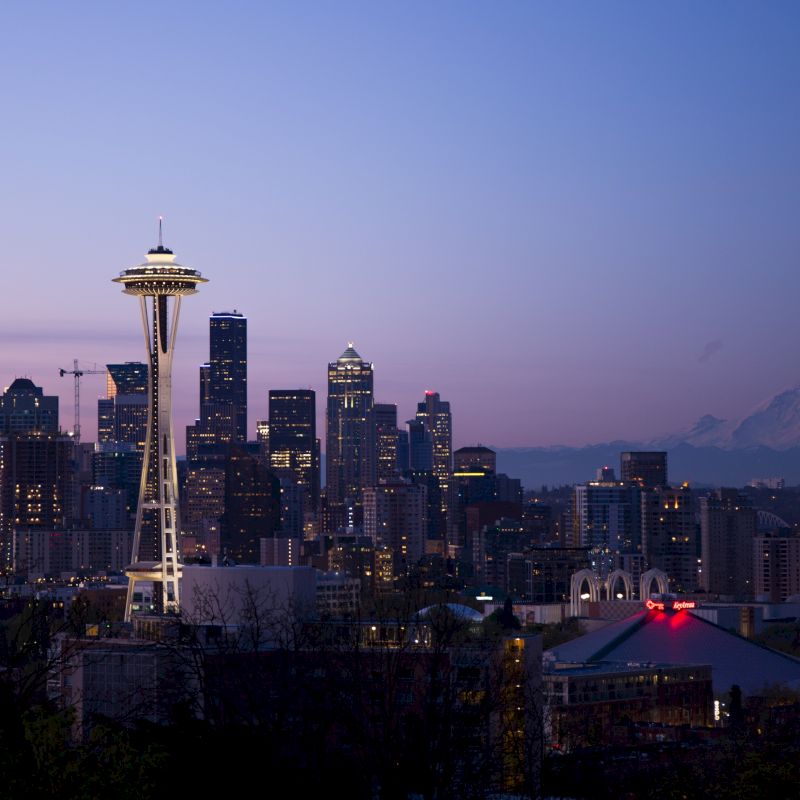 Seattle skyline at dusk, featuring the Space Needle and downtown buildings, with Mount Rainier in the background under a twilight sky.
