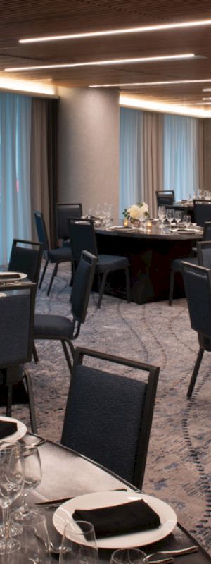 A banquet hall with round tables set for an event, featuring dark chairs, elegant table settings, and soft lighting.