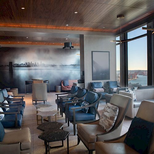 A modern lounge with plush seating, large windows offering ocean views, and a stylish mural on the wall.