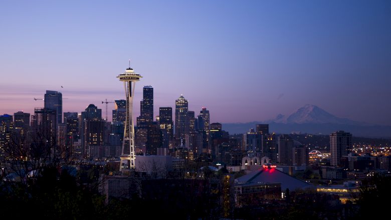 Seattle skyline at dusk with the Space Needle illuminated against a purple sky, and Mount Rainier visible in the distance.